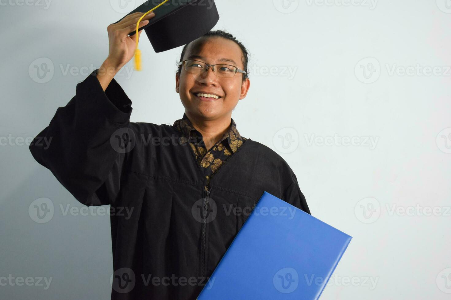 expressief van volwassen Indonesië mannetje slijtage diploma uitreiking gewaad, hoed en bril, Aziatisch mannetje diploma uitreiking brengen blanco blauw certificaat geïsoleerd Aan wit achtergrond, uitdrukkingen van portret diploma uitreiking foto