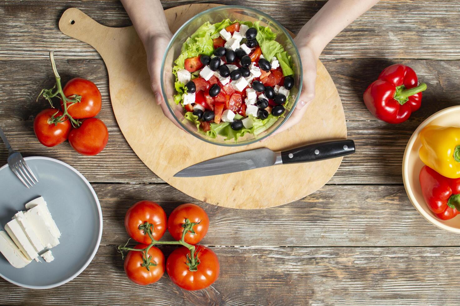 handen met een vegetarische salade in een glasplaat, gesneden gezonde voedselingrediënten op een houten tafel achtergrond, close-up foto