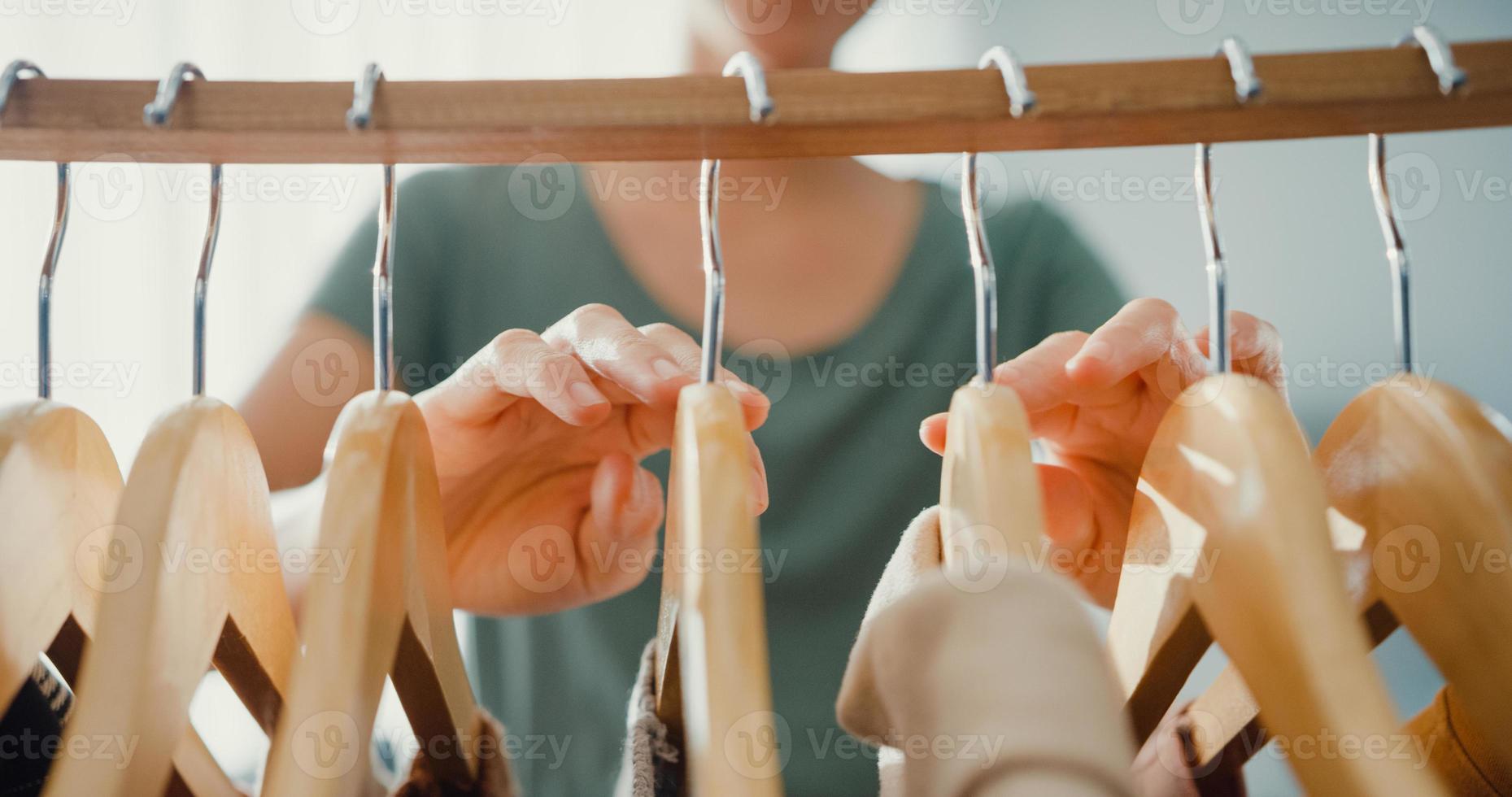 mooie aantrekkelijke jonge aziatische dame die haar mode-outfit kleding kiest in de woonkamer van de kast in huis of winkel. meisje denk wat te casual shirt te dragen. thuis garderobe of kledingwinkel kleedkamer. foto