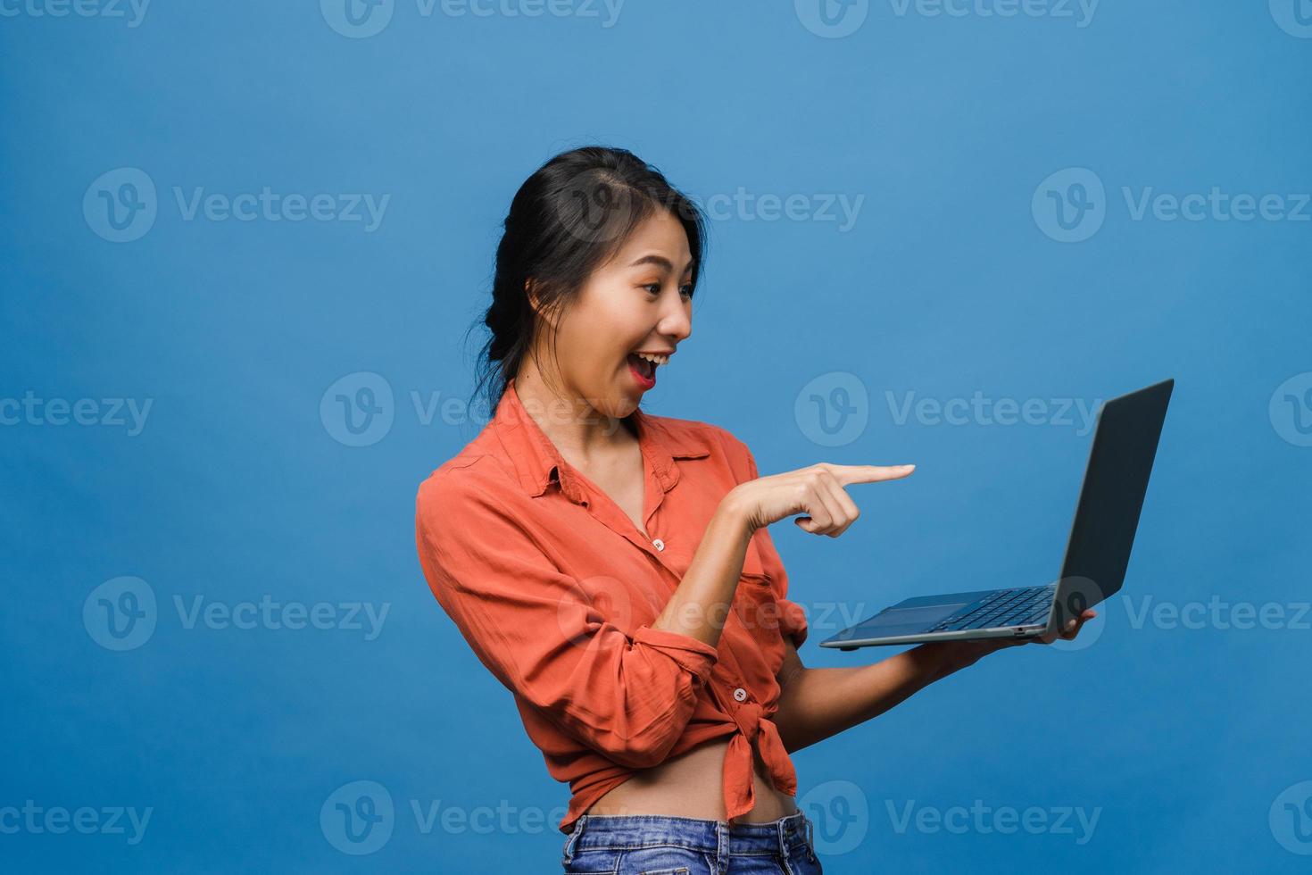 jonge aziatische dame die laptop gebruikt met positieve uitdrukking, breed glimlacht, gekleed in casual kleding die geluk voelt en geïsoleerd op blauwe achtergrond staat. gelukkige schattige blije vrouw verheugt zich over succes. foto