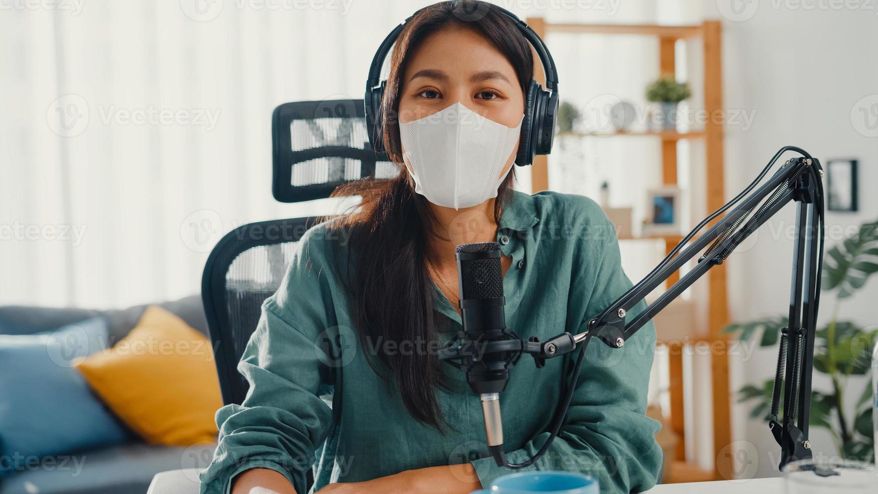 tiener azië meisje record podcast gebruik koptelefoon en microfoon draag masker bescherm virus kijk naar camera praten in haar kamer. vrouwelijke podcaster maakt audiopodcast vanuit haar thuisstudio, blijf thuis concept. foto