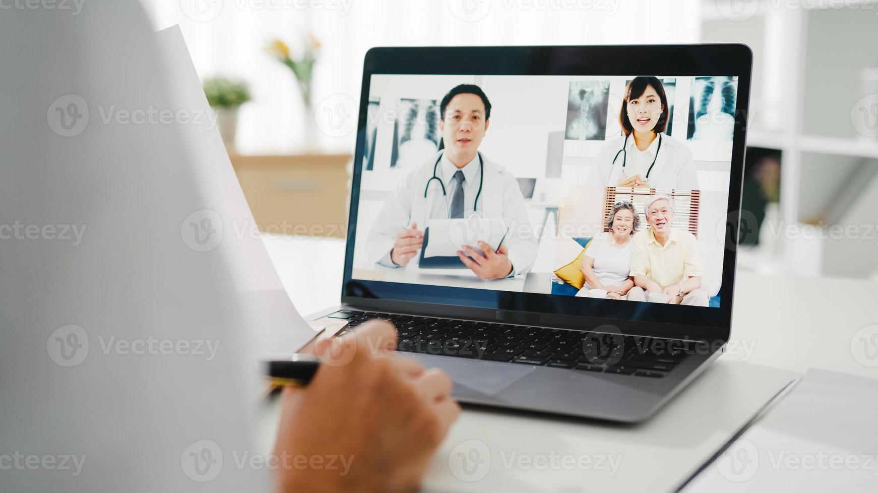 jonge Aziatische dame arts in wit medisch uniform met stethoscoop met behulp van computerlaptop praten videoconferentiegesprek met patiënt aan balie in gezondheidskliniek of ziekenhuis. advies- en therapieconcept. foto