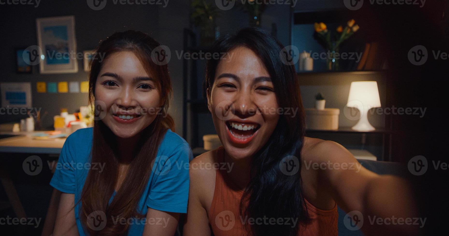 tiener azië vrouwen voelen zich gelukkig lachend selfie en kijken naar de camera met ontspannen in de woonkamer thuis 's nachts. vrolijke kamergenoot dames videogesprek met vriend en familie, lifestyle vrouw thuis concept. foto