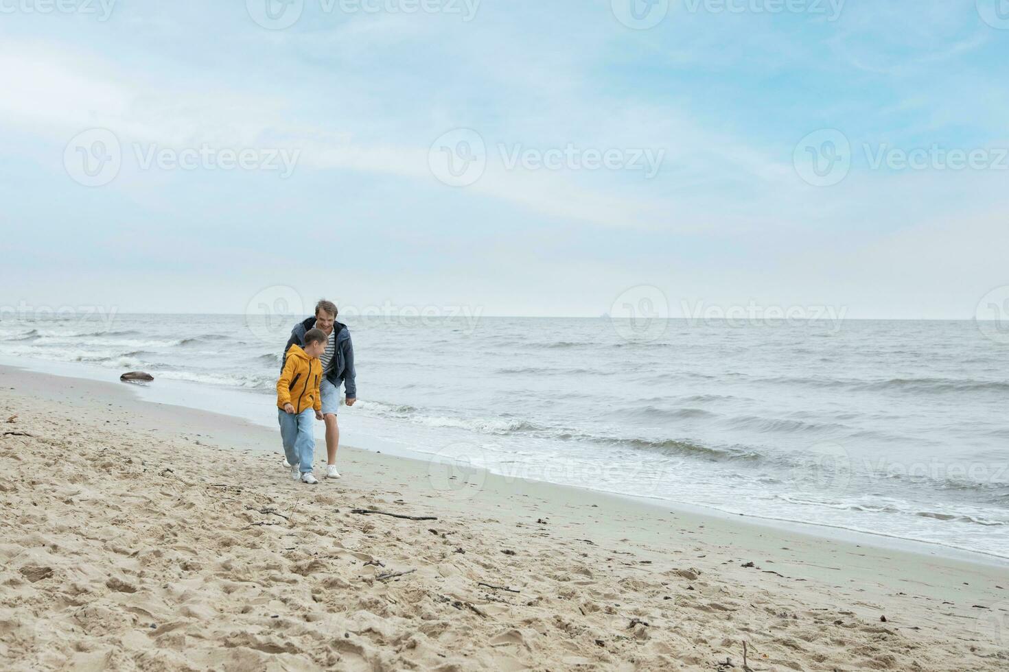 vader en zijn zoon rennen Aan de strand. koel herfst het weer. foto