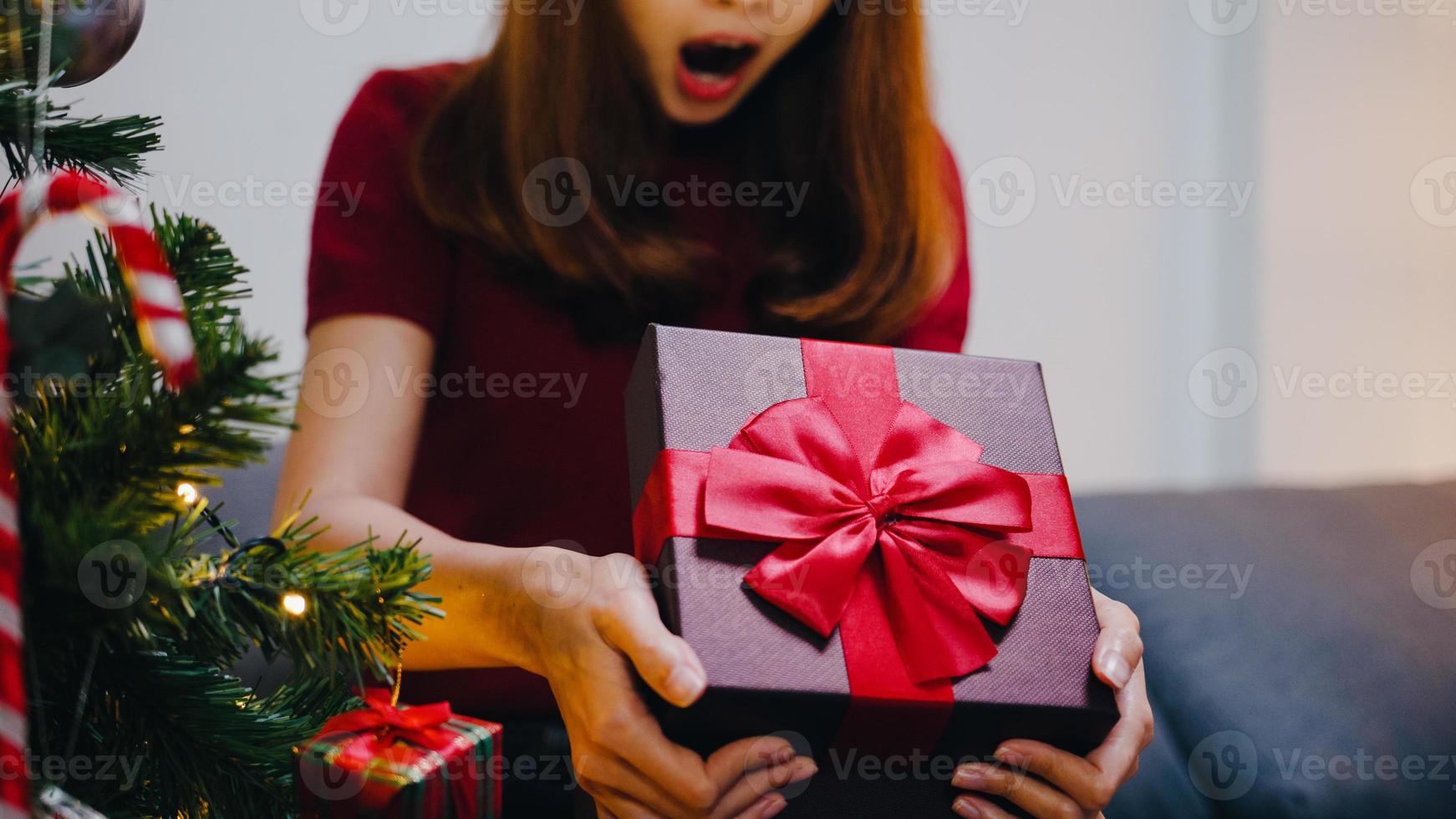 jonge azië vrouw plezier openen x'mas huidige doos in de buurt van kerstboom versierd met ornamenten in de woonkamer thuis. prettige kerstnacht en gelukkig nieuwjaar vakantie festival. foto