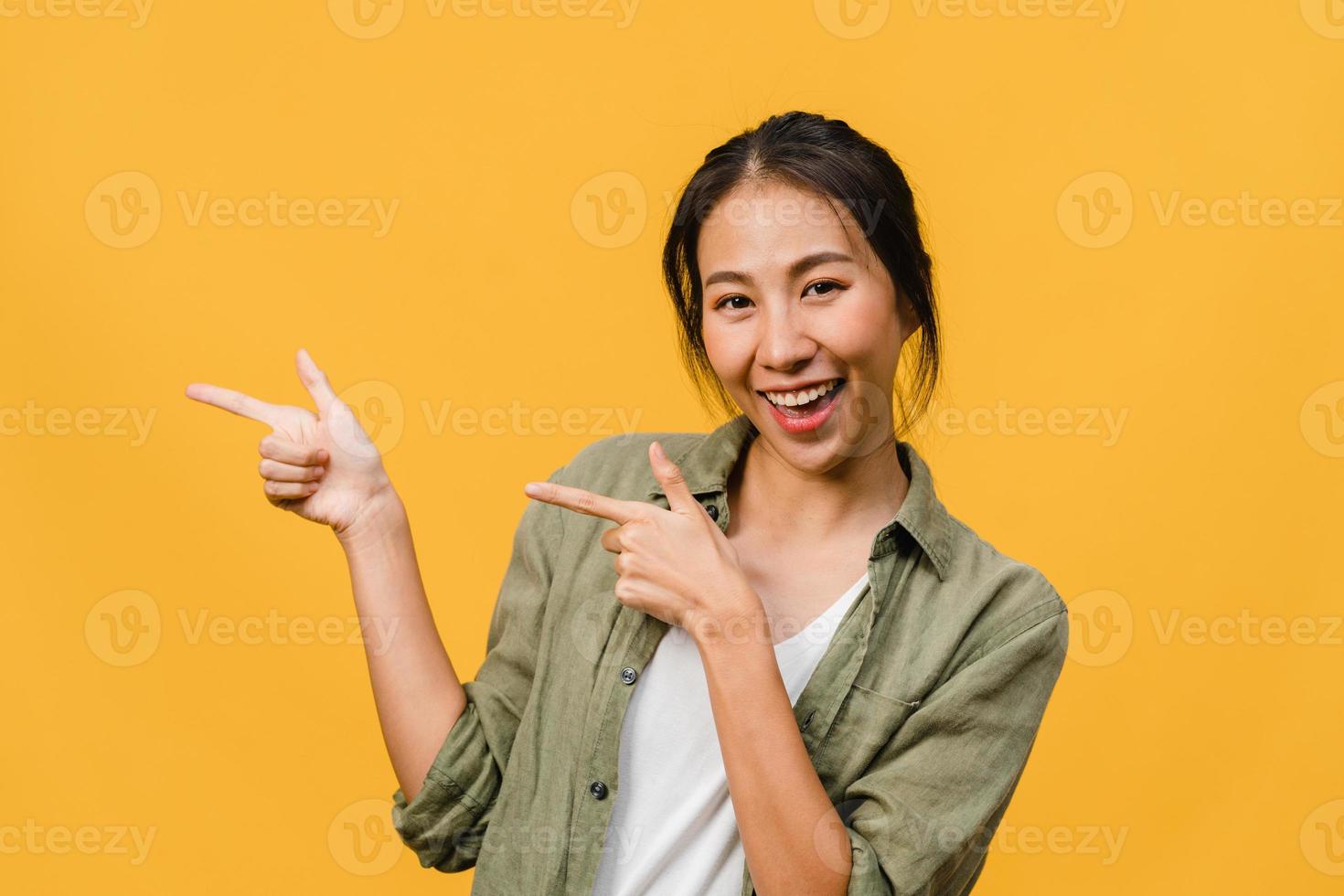portret van een jonge aziatische dame die lacht met een vrolijke uitdrukking, laat iets geweldigs zien op lege ruimte in casual doek en kijkt naar camera geïsoleerd over gele achtergrond. gezichtsuitdrukking concept. foto
