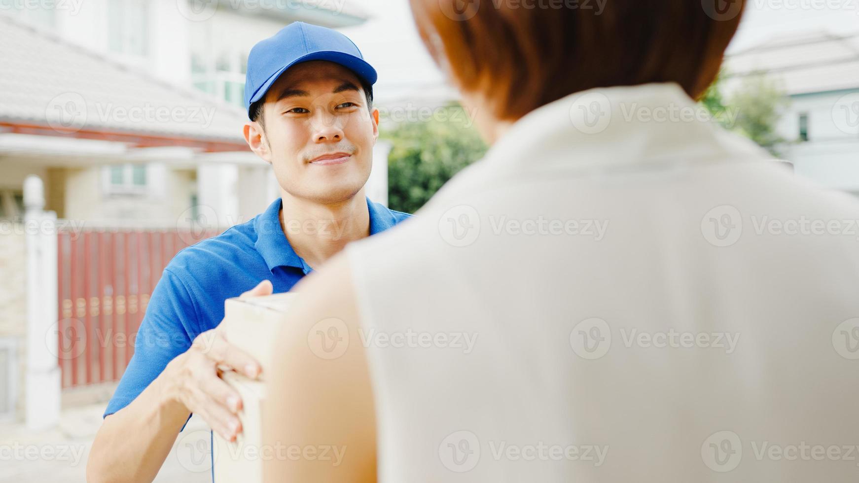 jonge azië postbezorgingskoerier man in blauw shirt die pakketdozen hanteert voor verzending naar de klant thuis en aziatische vrouw ontvangt geleverd pakket buitenshuis. pakket winkelen eten levering concept. foto