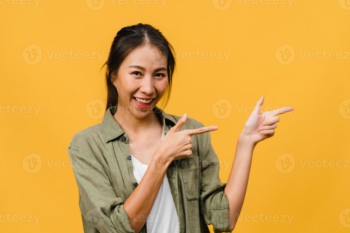 portret van een jonge aziatische dame die lacht met een vrolijke uitdrukking, laat iets geweldigs zien op lege ruimte in casual doek en kijkt naar camera geïsoleerd over gele achtergrond. gezichtsuitdrukking concept. foto