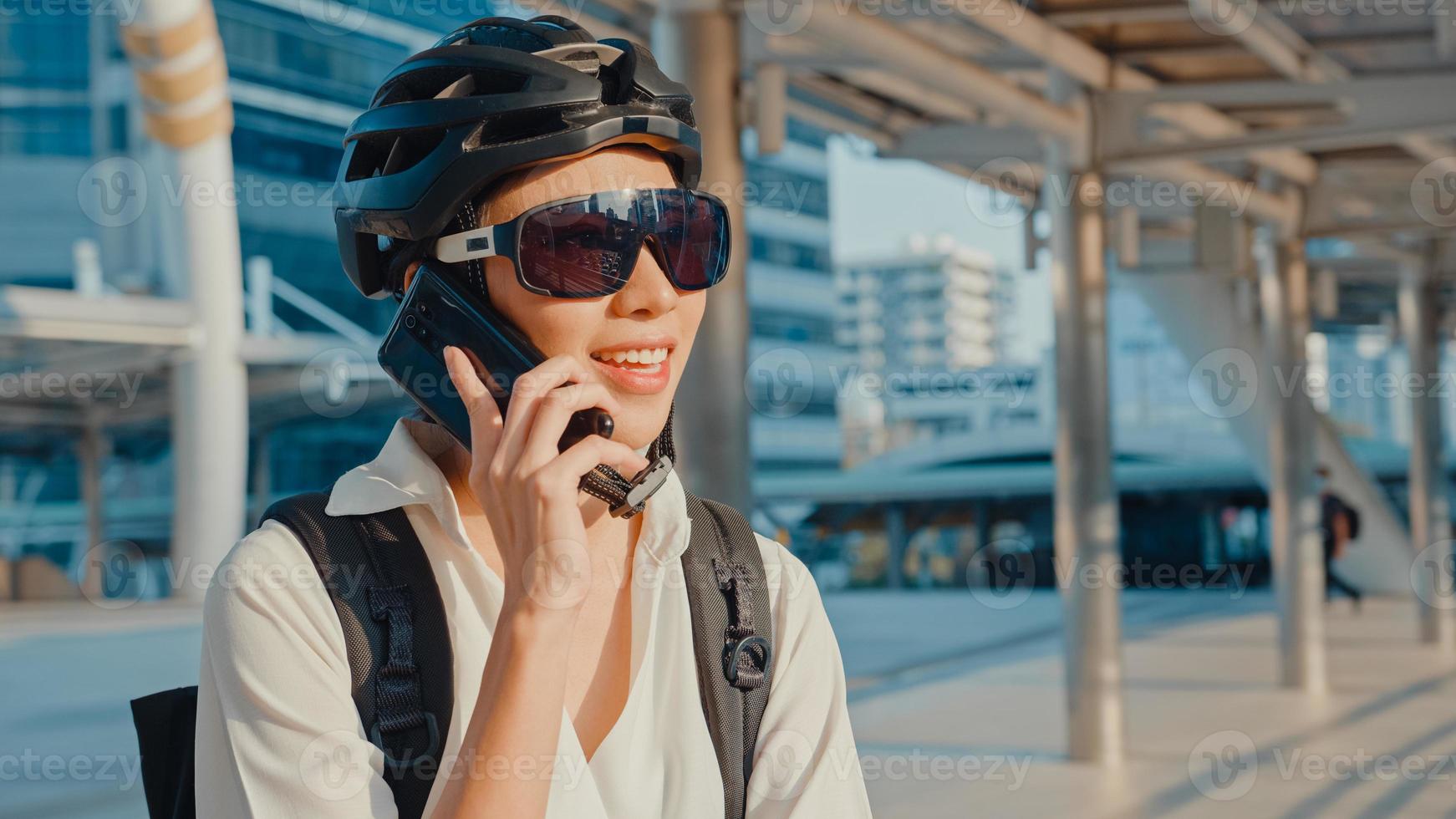 Aziatische zakenvrouw met rugzak bellen mobiel praten lachend in de stad straat gaan werken op kantoor. sportmeisje gebruikt haar telefoon voor werk. pendelen naar het werk met de fiets, zakelijke forens in de stad. foto