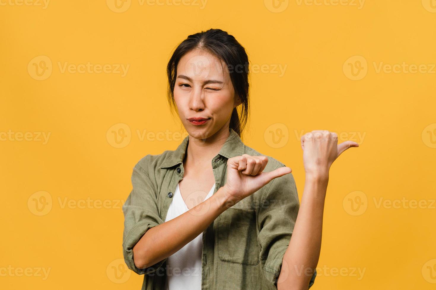 portret van een jonge aziatische dame die lacht met een vrolijke uitdrukking, laat iets geweldigs zien op lege ruimte in casual doek en kijkt naar camera geïsoleerd over gele achtergrond. gezichtsuitdrukking concept. foto