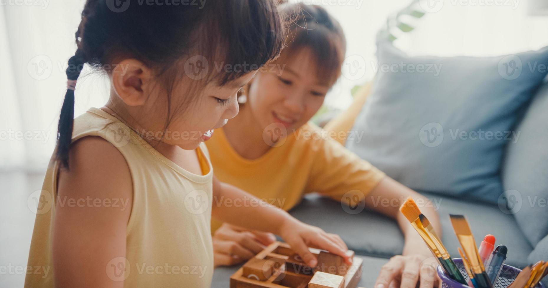 gelukkige vrolijke azië familie moeder leert meisje bordspel hobby spelen met houten kist plezier ontspannen op de bank in de woonkamer thuis. tijd samen doorbrengen, sociale afstand, quarantaine voor coronavirus. foto