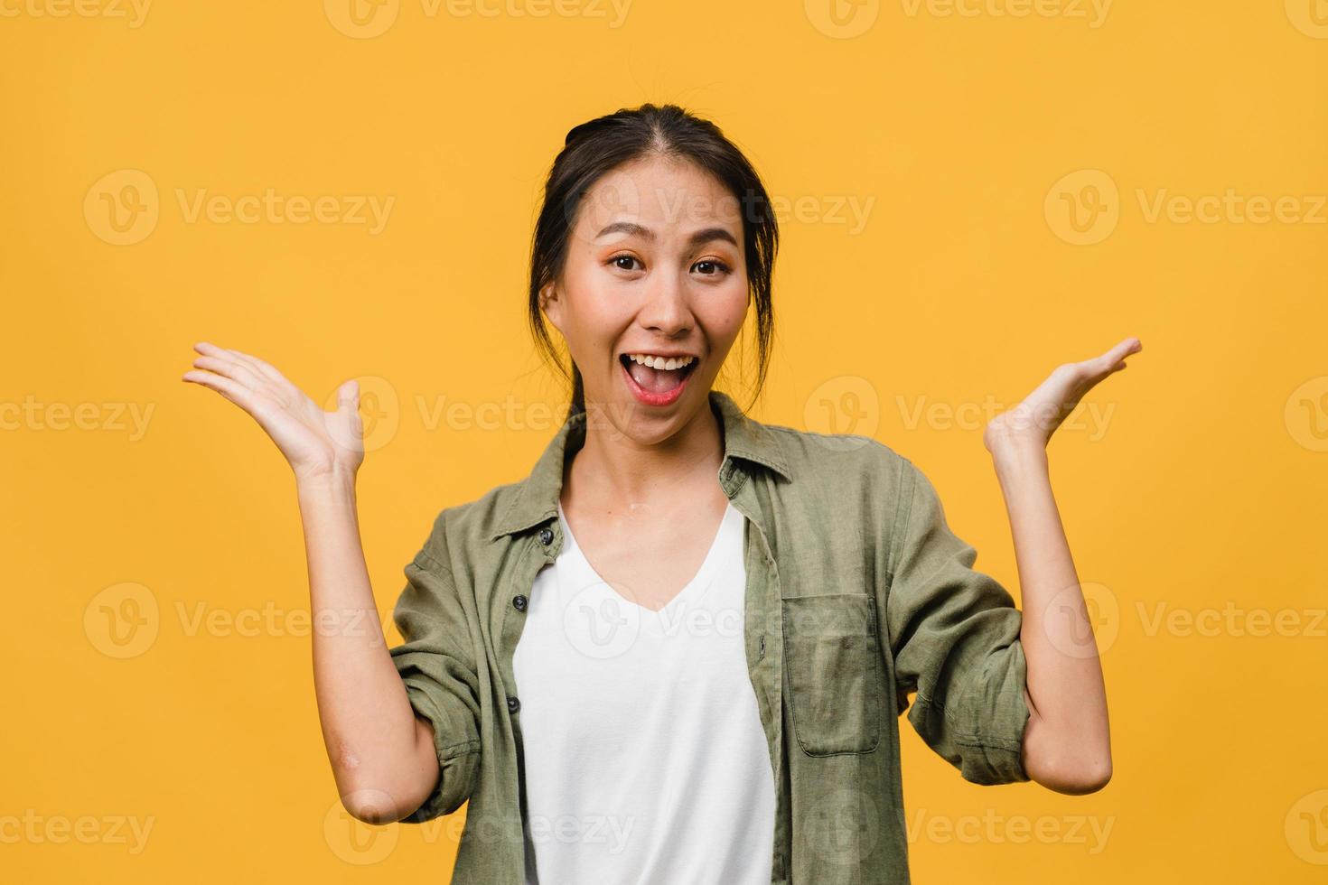 jonge Aziatische dame voelt geluk met positieve uitdrukking, vrolijke verrassing funky, gekleed in casual doek en kijkend naar camera geïsoleerd op gele achtergrond. gelukkige schattige blije vrouw verheugt zich over succes. foto
