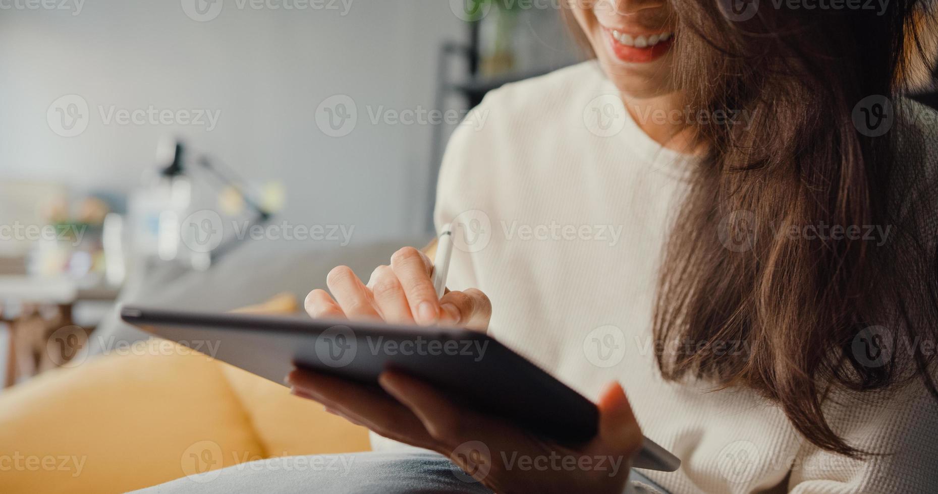 close-up freelance azië dame vrijetijdskleding met behulp van tablet online leren in de woonkamer thuis. thuiswerken, werken op afstand, onderwijs op afstand, sociale afstand, quarantaine voor preventie van het coronavirus. foto