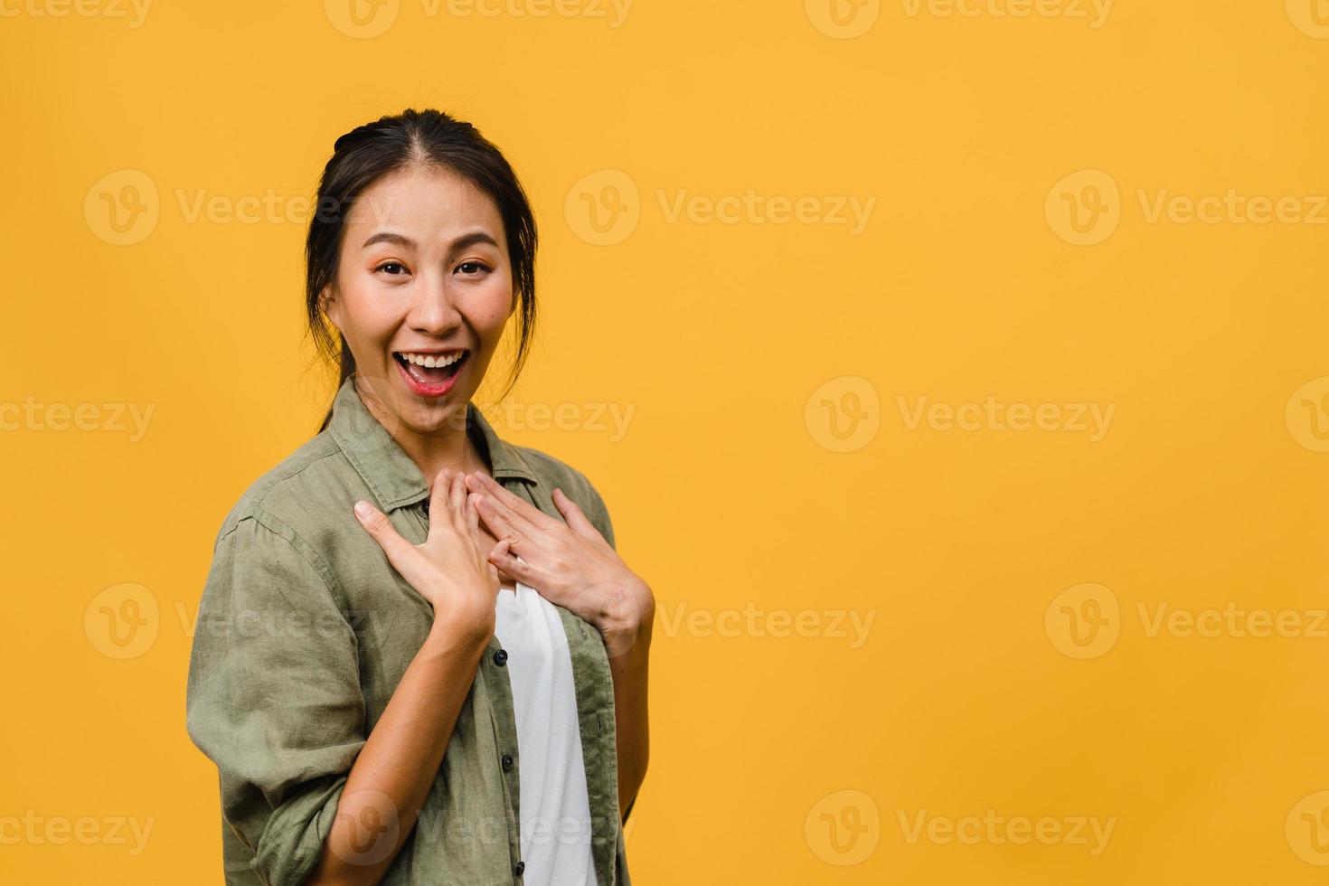 jonge Aziatische dame voelt geluk met positieve uitdrukking, vrolijke verrassing funky, gekleed in casual doek en kijkend naar camera geïsoleerd op gele achtergrond. gelukkige schattige blije vrouw verheugt zich over succes. foto