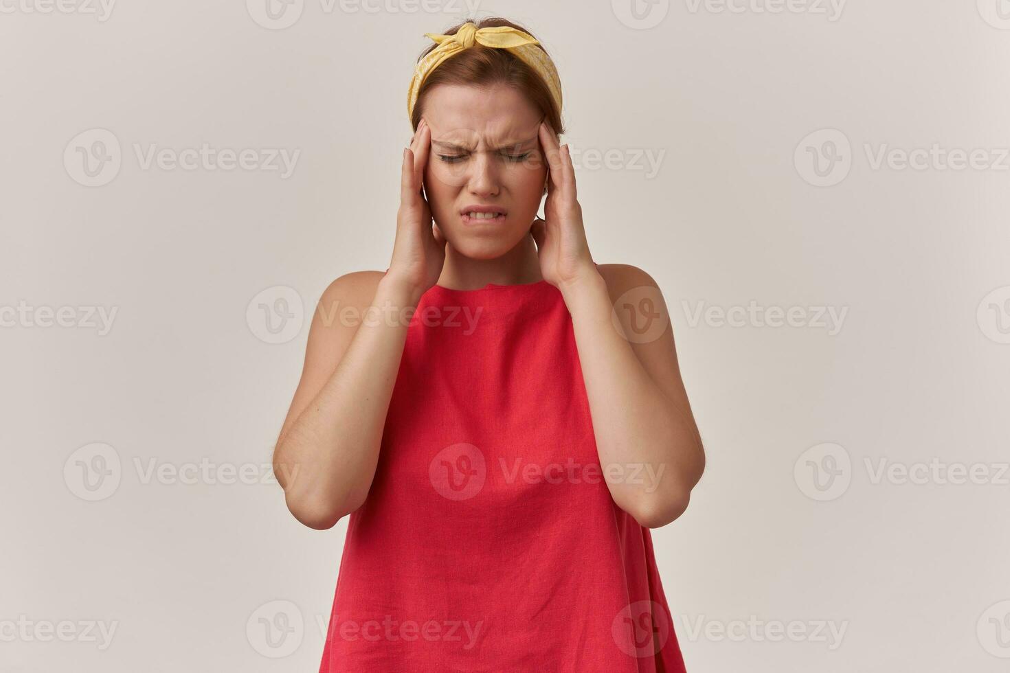 beeld van Europese bruin haren jeugd vrouw in elegant modieus rood jurk en geel bandana met armen aanraken gezicht en ogen Gesloten emotie benadrukt in pijn hoofdpijn poseren tegen wit achtergrond foto