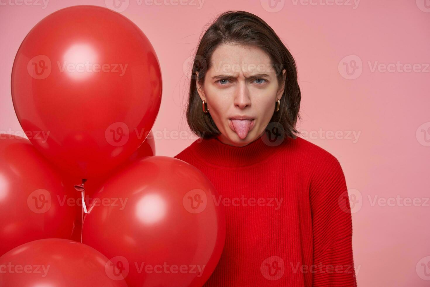 binnen- portret van jong verdrietig brunette vrouw, tonen haar tong. geïsoleerd over- roze achtergrond. foto