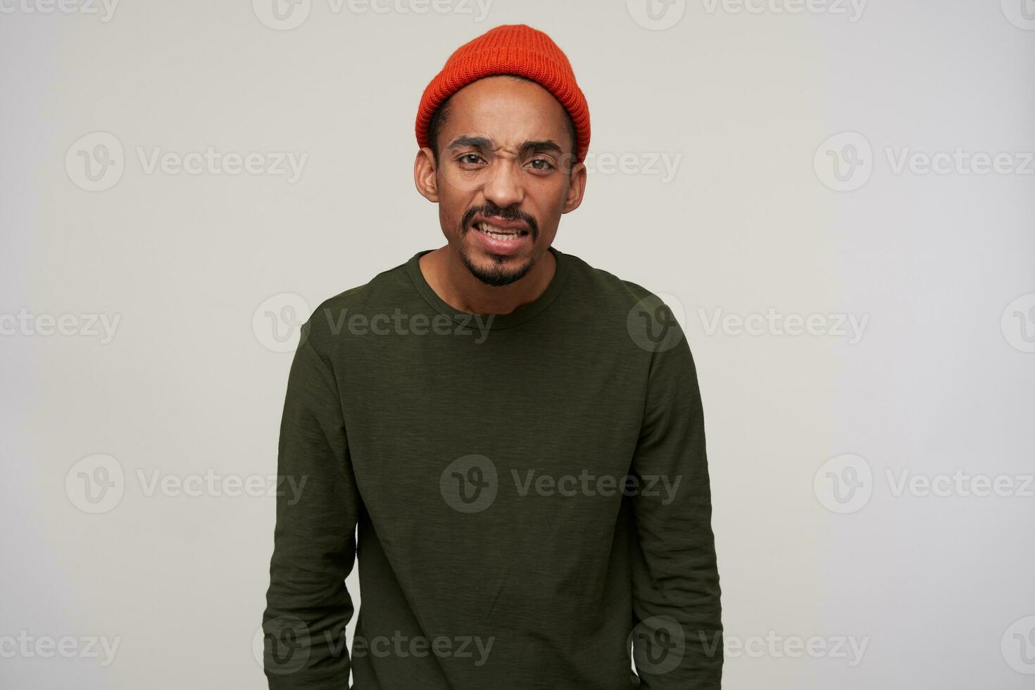 niet tevreden jong aantrekkelijk bruine ogen donker huid brunette mannetje met baard fronsend zijn gezicht en op zoek naar camera met steenbolk, geïsoleerd over- wit achtergrond foto