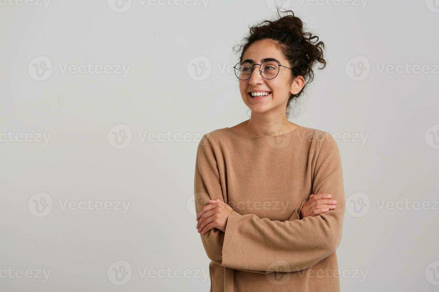 portret van aantrekkelijk, volwassen meisje met donker gekruld haar- broodje. vervelend beige jumper en bril. emotie concept. houdt armen gekruist. aan het kijken naar de links Bij kopiëren ruimte, geïsoleerd over- wit achtergrond foto