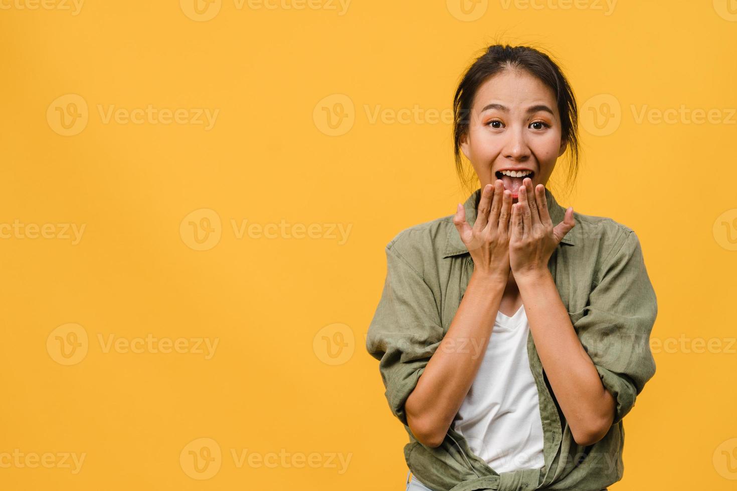 jonge Aziatische dame voelt geluk met positieve uitdrukking, vrolijke verrassing funky, gekleed in casual doek en kijkend naar camera geïsoleerd op gele achtergrond. gelukkige schattige blije vrouw verheugt zich over succes. foto
