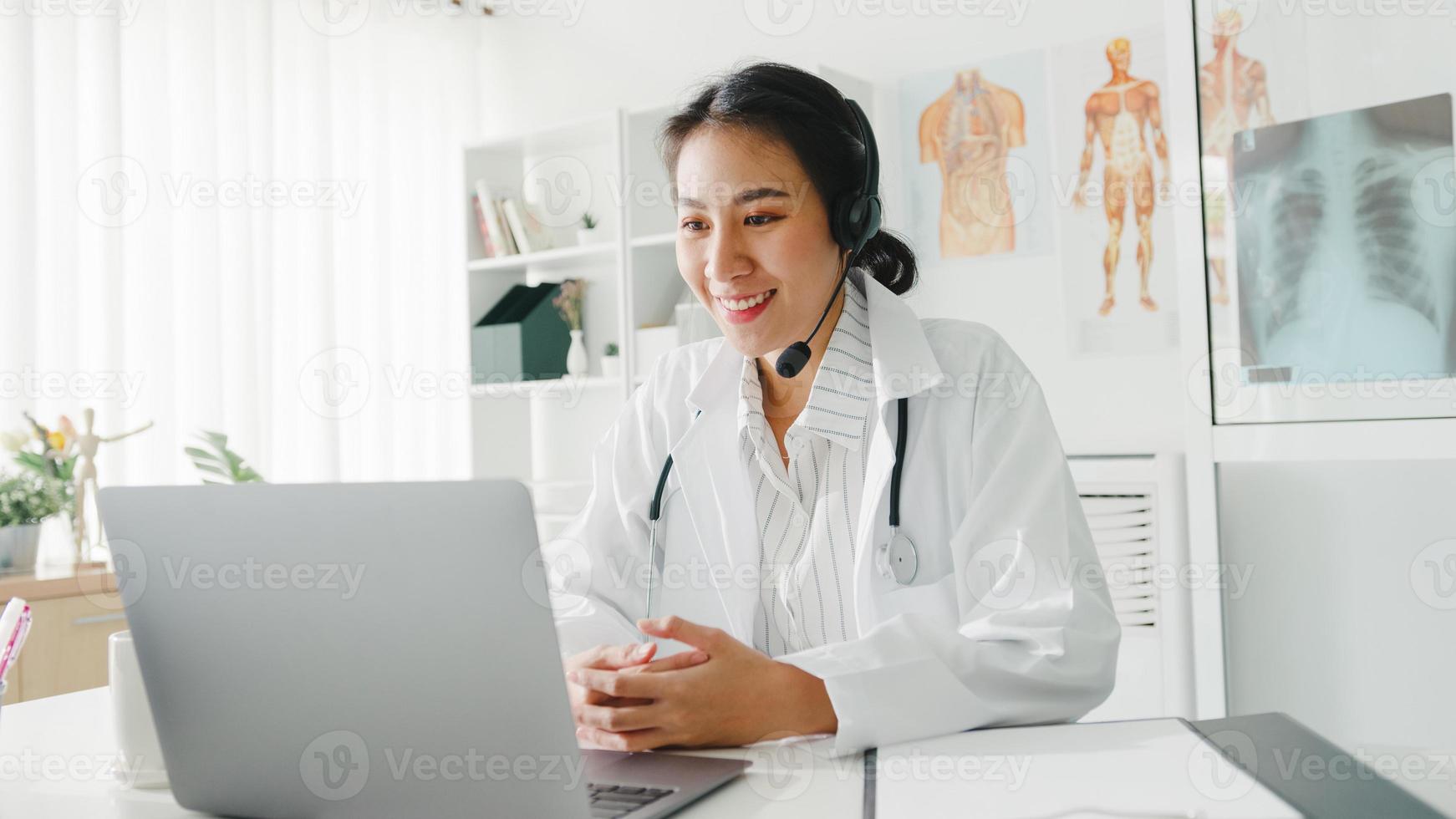 jonge Aziatische dame arts in wit medisch uniform met stethoscoop met behulp van computerlaptop praten videoconferentiegesprek met patiënt aan balie in gezondheidskliniek of ziekenhuis. advies- en therapieconcept. foto