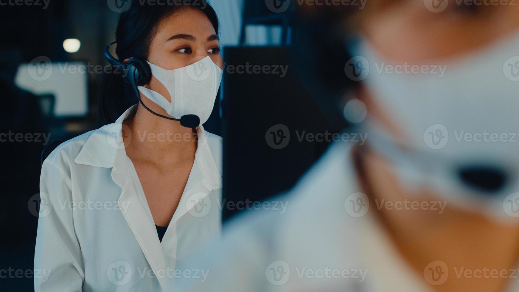 millennial azië jong callcenterteam of klantenservicemedewerker die gezichtsmasker draagt, voorkomt covid-19 met behulp van computer en microfoonheadset die technische ondersteuning biedt in het late nachtkantoor. foto