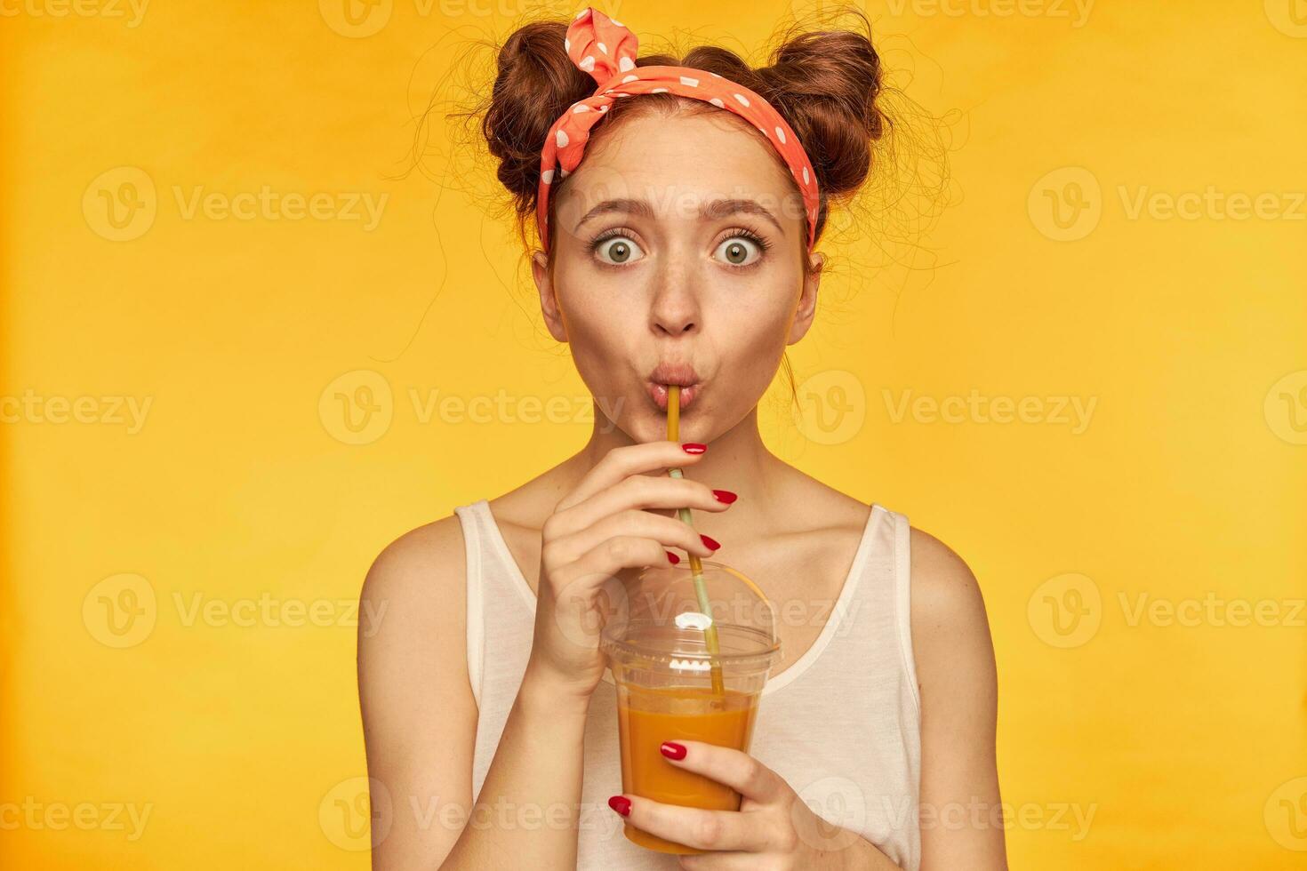 portret van verrast, rood haar- meisje met rood verliefd haarband. geschokt met smaak, maken een slokje. vervelend wit overhemd en Holding haar smoothie. aan het kijken Bij de camera geïsoleerd over- geel achtergrond foto