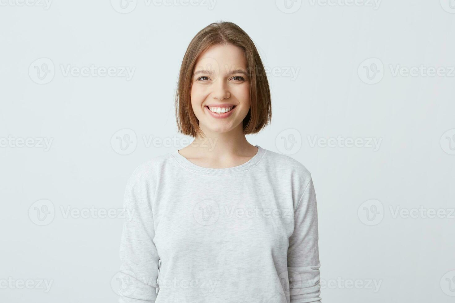 mooi vrouw drukt uit gelukkig emoties, heeft breed aangenaam glimlach, draagt wit lang mouw en voelt tevreden. geïsoleerd over- wit achtergrond foto