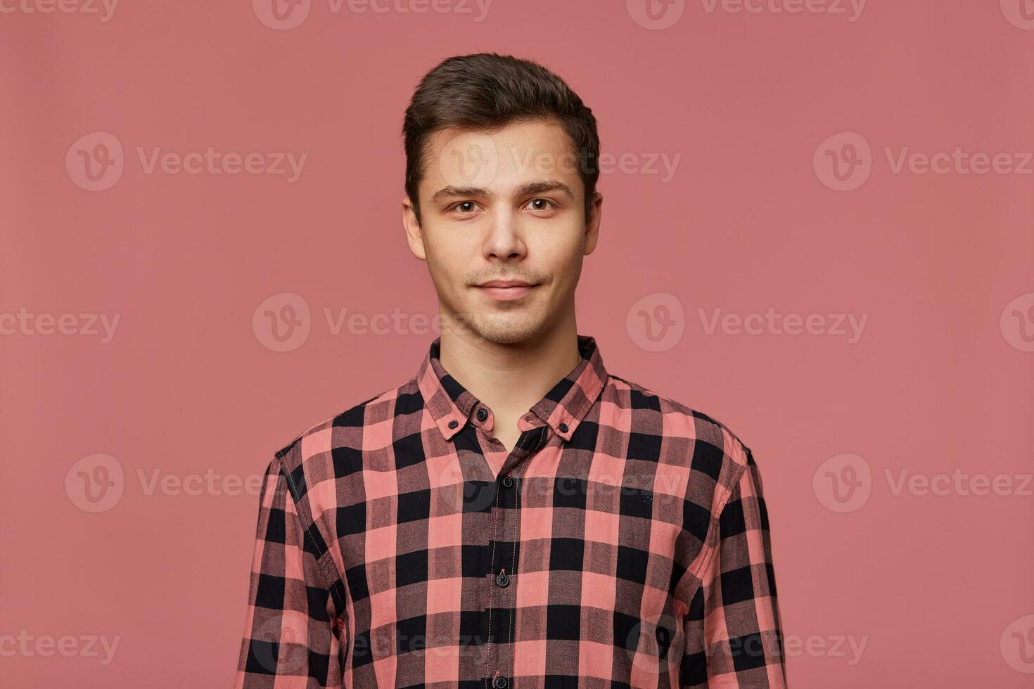 portret van jong aantrekkelijk Mens in geruit shirt, rustig looks Bij de camera, staat over- roze achtergrond. foto