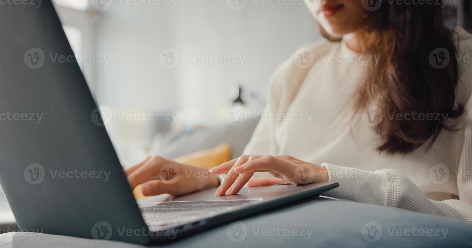 close-up freelance azië dame vrijetijdskleding met behulp van laptop online leren in de woonkamer thuis. thuiswerken, op afstand, onderwijs op afstand, social distancing, quarantaine voor coronaviruspreventie. foto