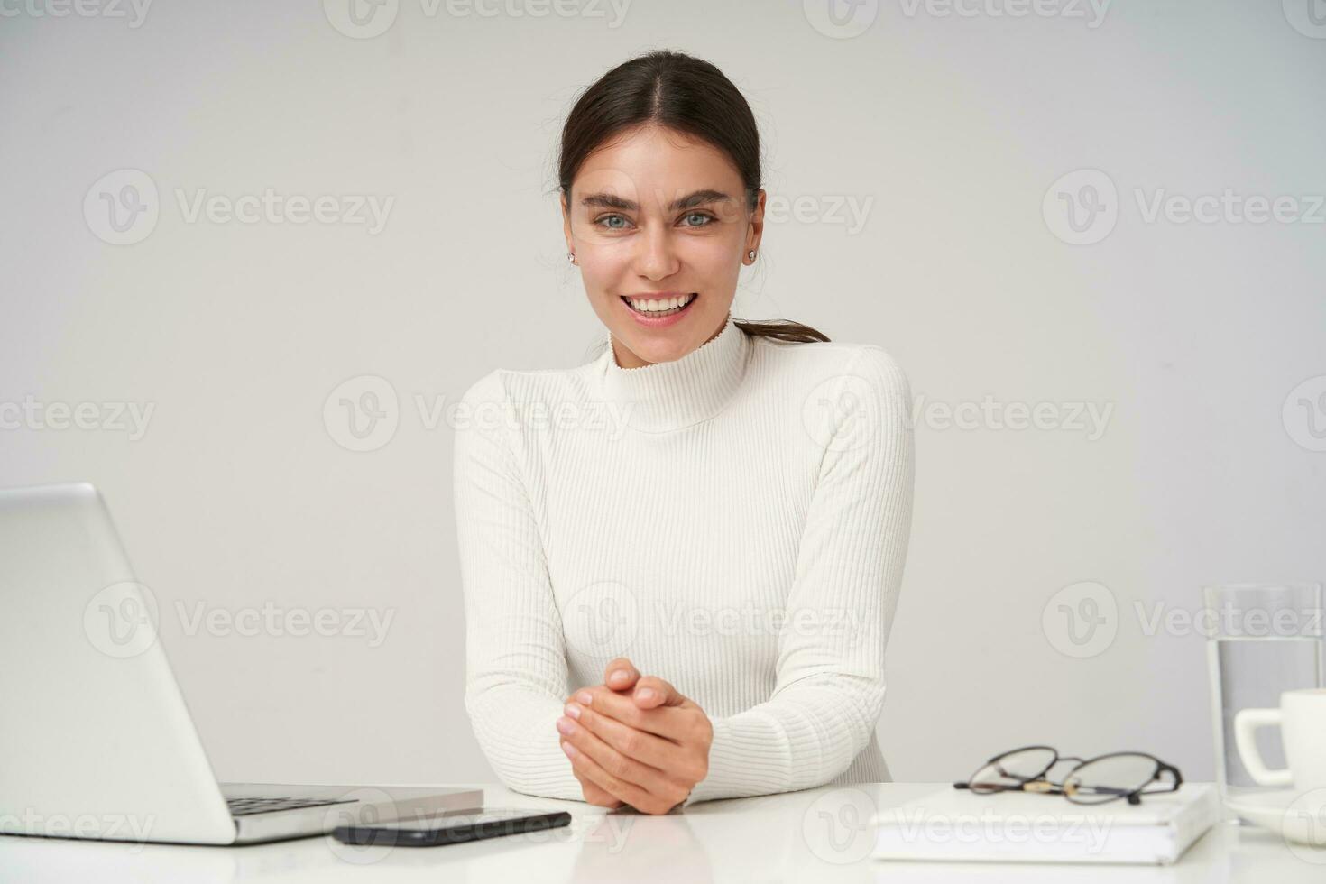 portret van blij jong lief brunette vrouw gekleed in wit Polo nek vouwen haar handen Aan aanrecht en op zoek positief Bij camera met oprecht glimlach, geïsoleerd over- wit achtergrond foto