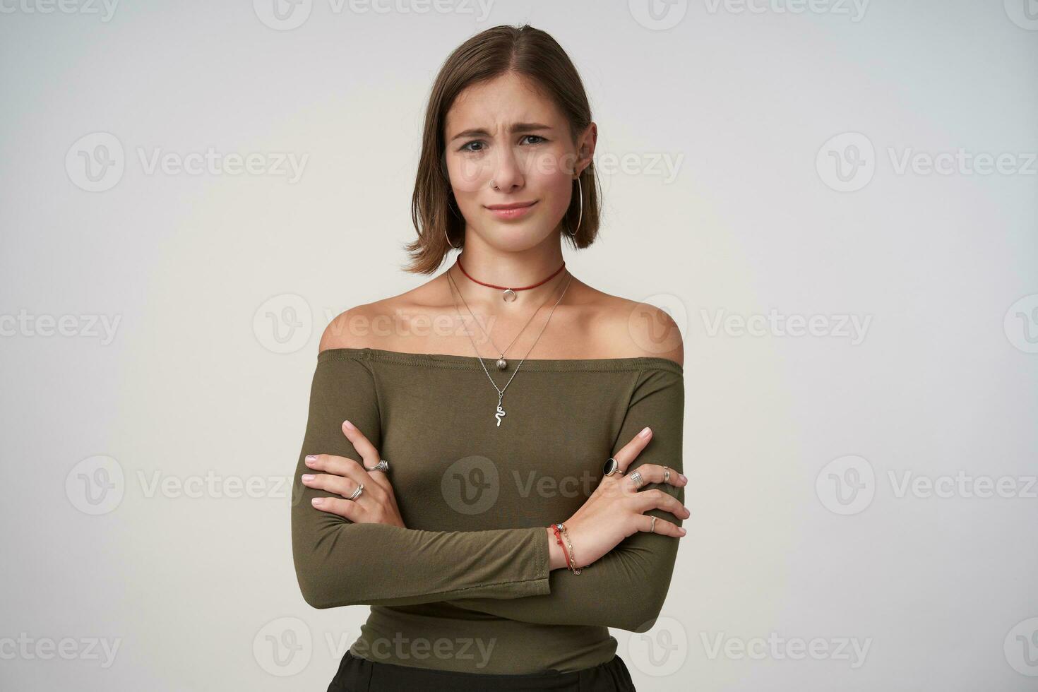 studio foto van jong aantrekkelijk kort haren dame met natuurlijk bedenken houden haar lippen gevouwen terwijl staand over- wit achtergrond met gekruiste handen