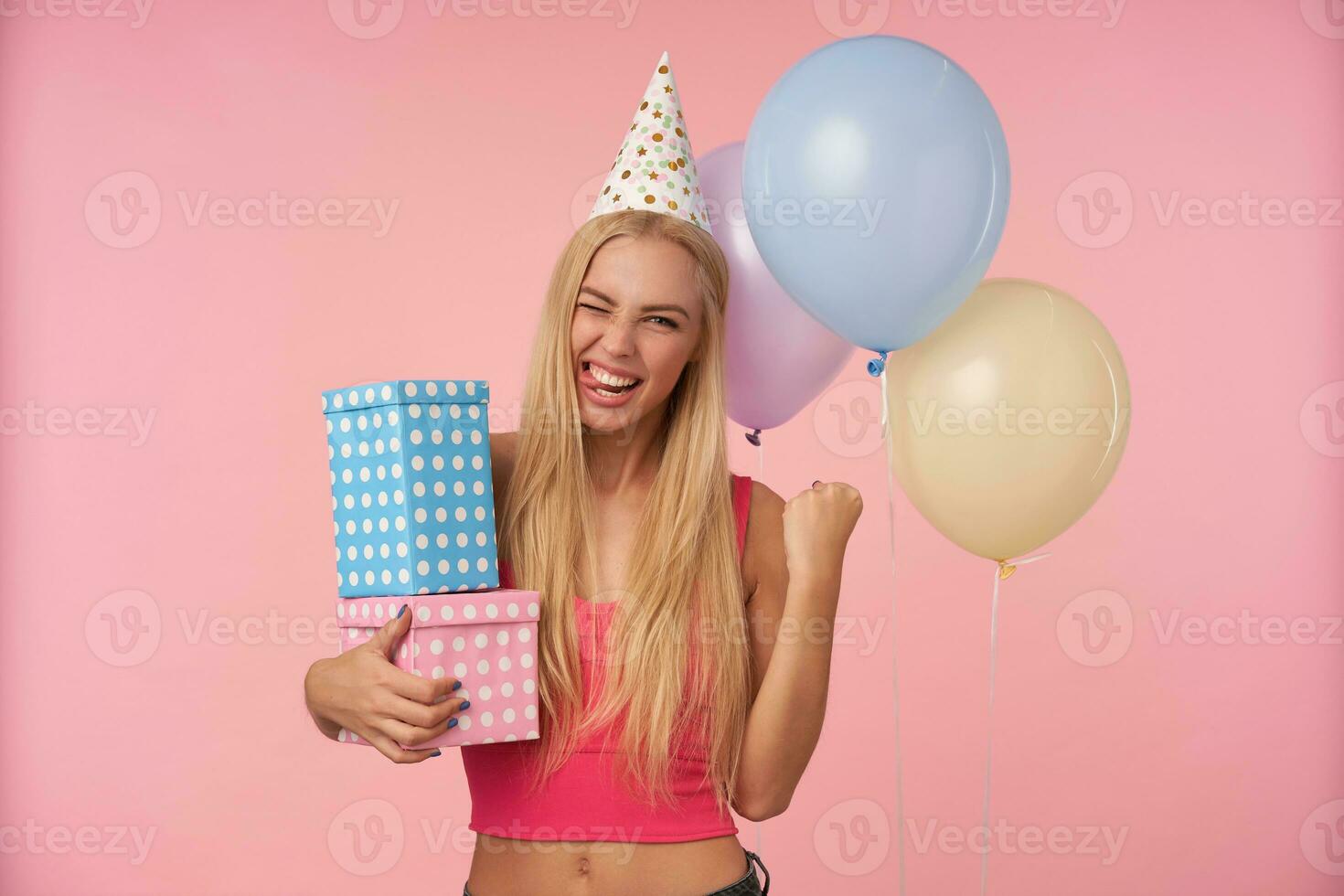 vrolijk mooi jong blond vrouw verheugt mooi hoor partij samen met vrienden, wezen in hoog geest en verhogen vuist gelukkig, geïsoleerd over- roze achtergrond en bundel van veelkleurig helium ballonnen foto