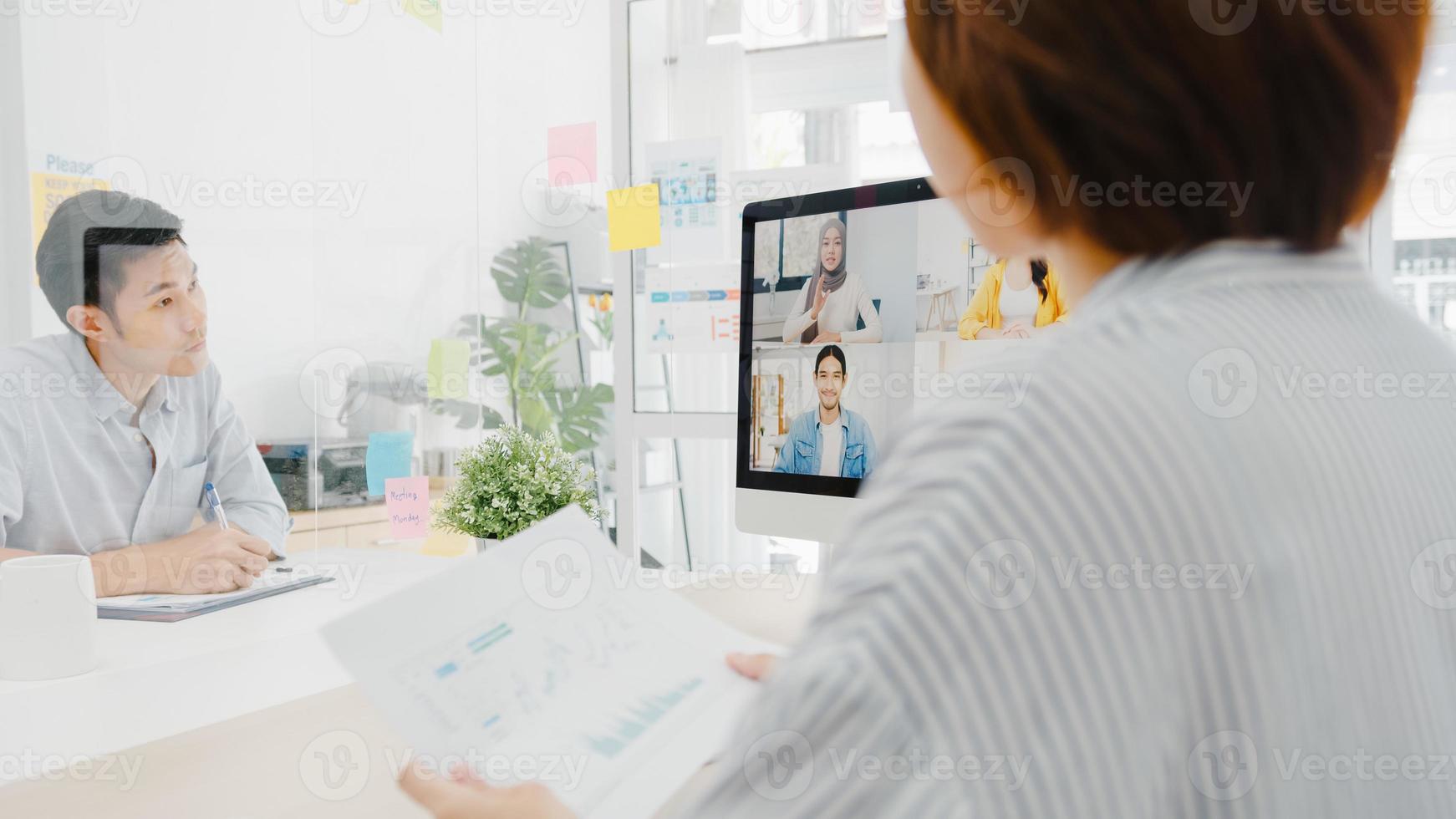 Aziatische zakenmensen die desktop gebruiken, praten met collega's die zakelijke brainstorm over plan bespreken in een videogesprekvergadering in een nieuw normaal kantoor. levensstijl sociale afstand en werk na het coronavirus. foto