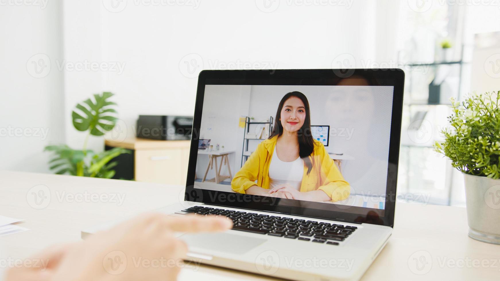 azië zakenvrouw met behulp van laptop praten met collega's over plan in videogesprek vergadering tijdens het werken vanuit huis in de woonkamer. zelfisolatie, sociale afstand, quarantaine voor preventie van het coronavirus. foto