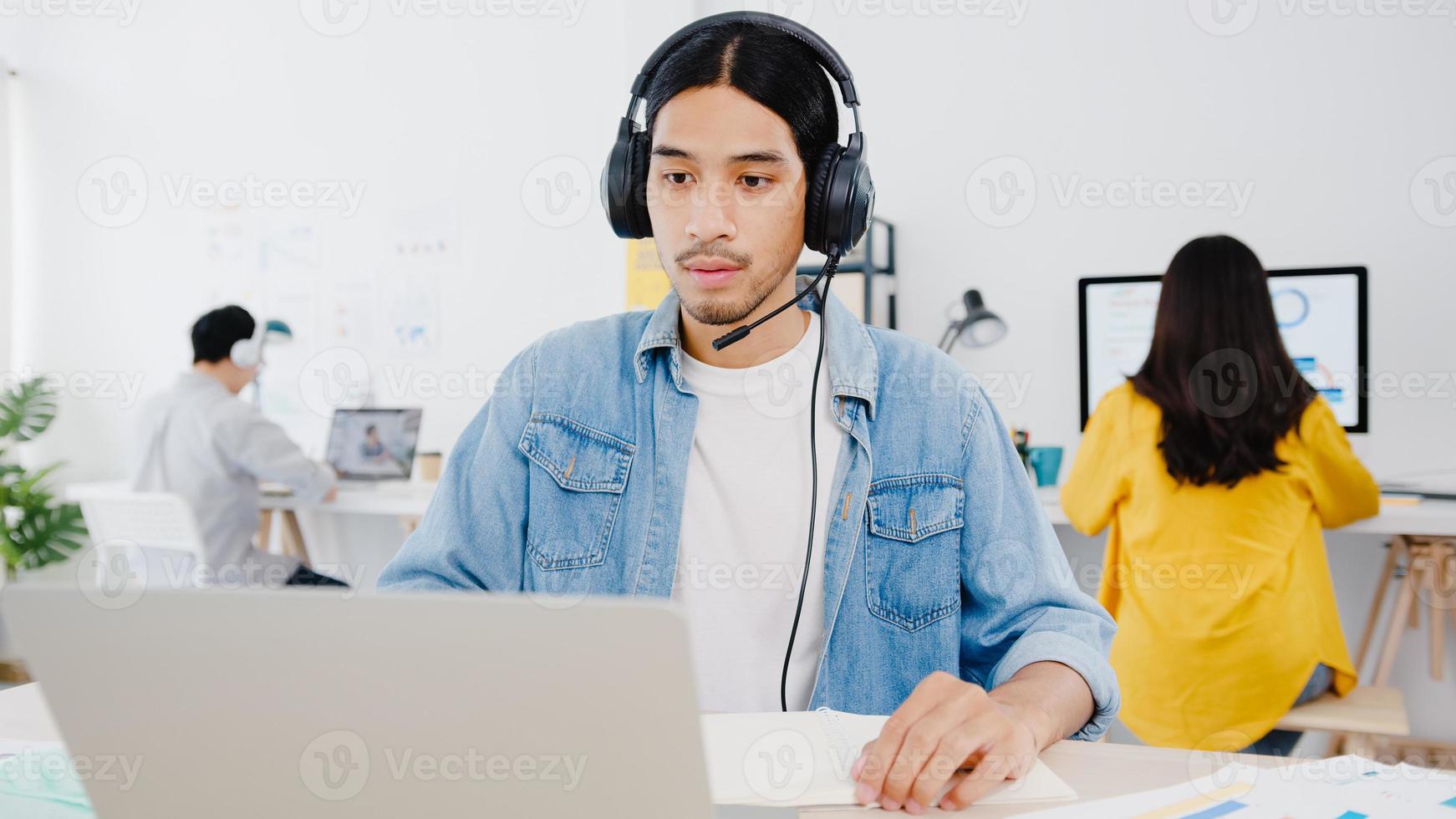 azië zakenman sociale afstand in nieuwe normale situatie voor viruspreventie met behulp van laptoppresentatie aan collega over plan in videogesprek tijdens het werk in een thuiskantoor. levensstijl na het coronavirus. foto