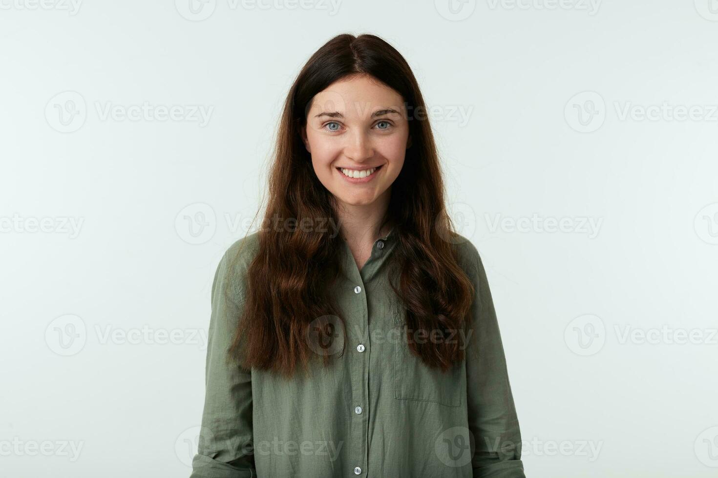 vrolijk jong mooi lang haren brunette vrouw tonen haar wit perfect tanden terwijl glimlachen gelukkig, gekleed in gewoontjes kleren terwijl poseren over- wit achtergrond foto