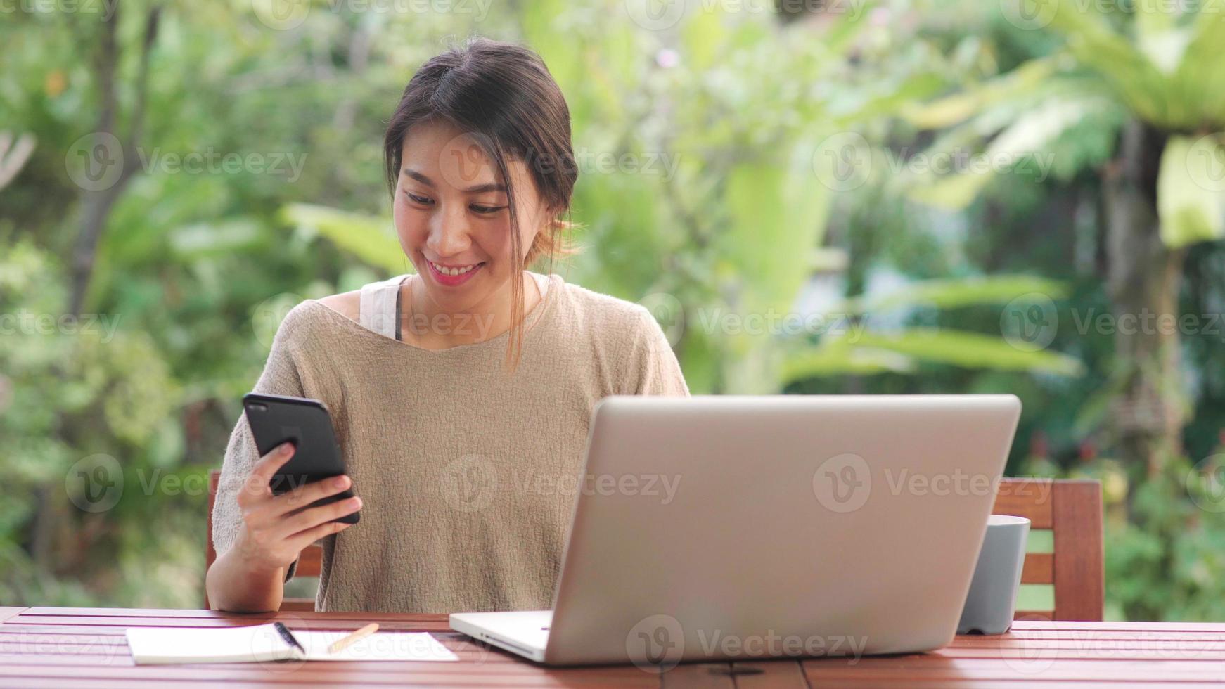 freelance aziatische vrouw die thuis werkt, zakelijke vrouw die op laptop werkt en mobiele telefoon gebruikt die koffie drinkt zittend op tafel in de tuin in de ochtend. levensstijl vrouwen die thuis werken concept. foto