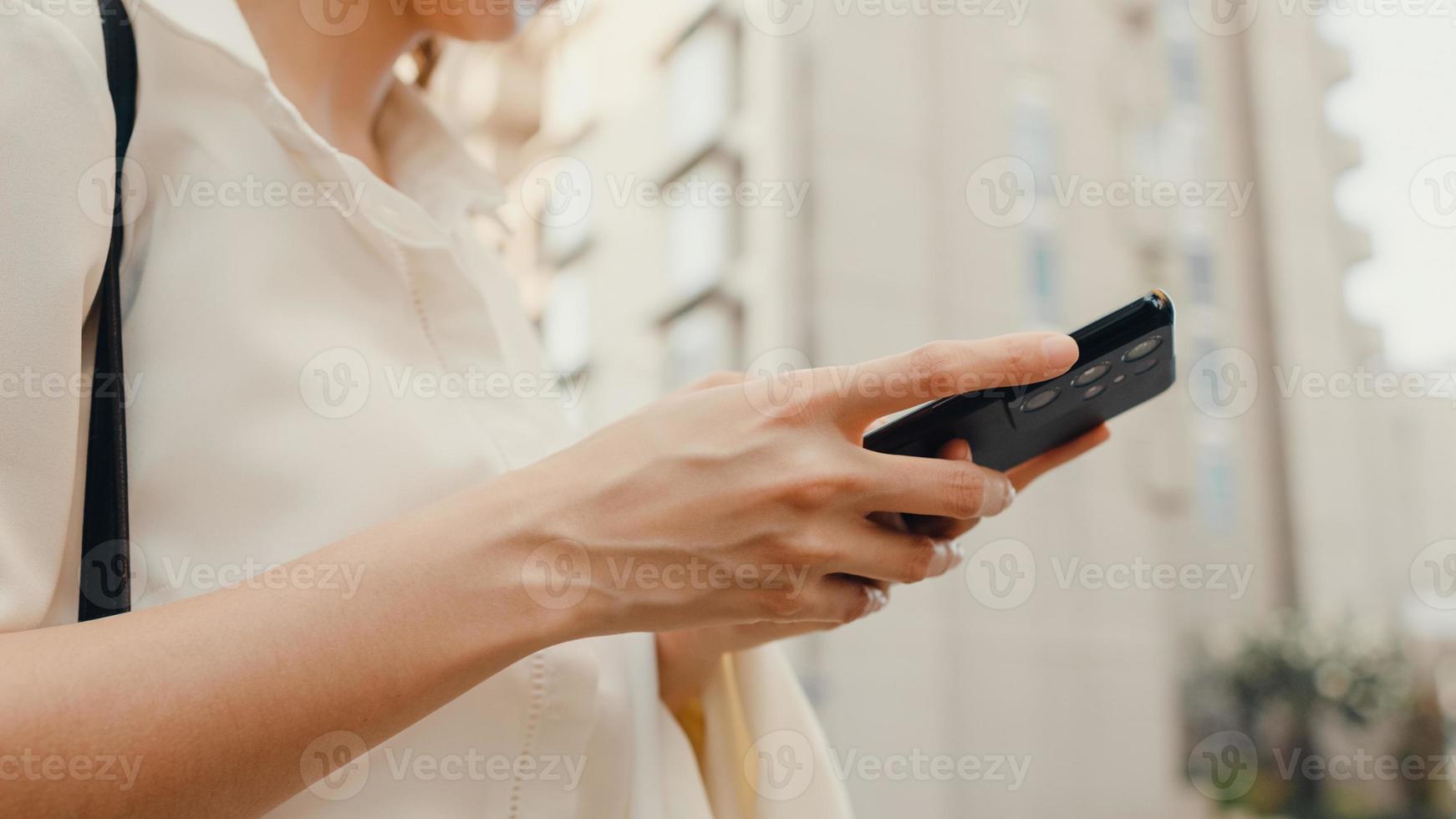 succesvolle jonge azië zakenvrouw in mode kantoorkleding met behulp van slimme telefoon en het typen van SMS-bericht terwijl ze alleen buiten wandelen in de stedelijke moderne stad in de ochtend. bedrijf onderweg concept. foto