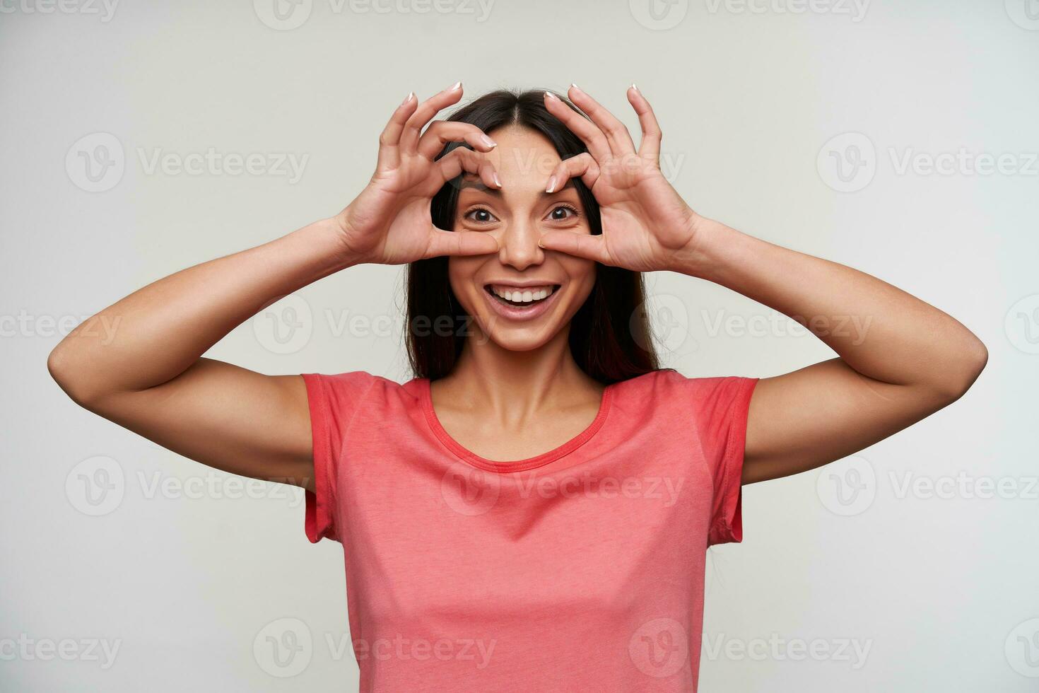 vrolijk jong aantrekkelijk bruine ogen brunette dame met natuurlijk bedenken verhogen handen naar haar gezicht en hebben pret terwijl poseren over- wit achtergrond in gewoontjes kleren foto