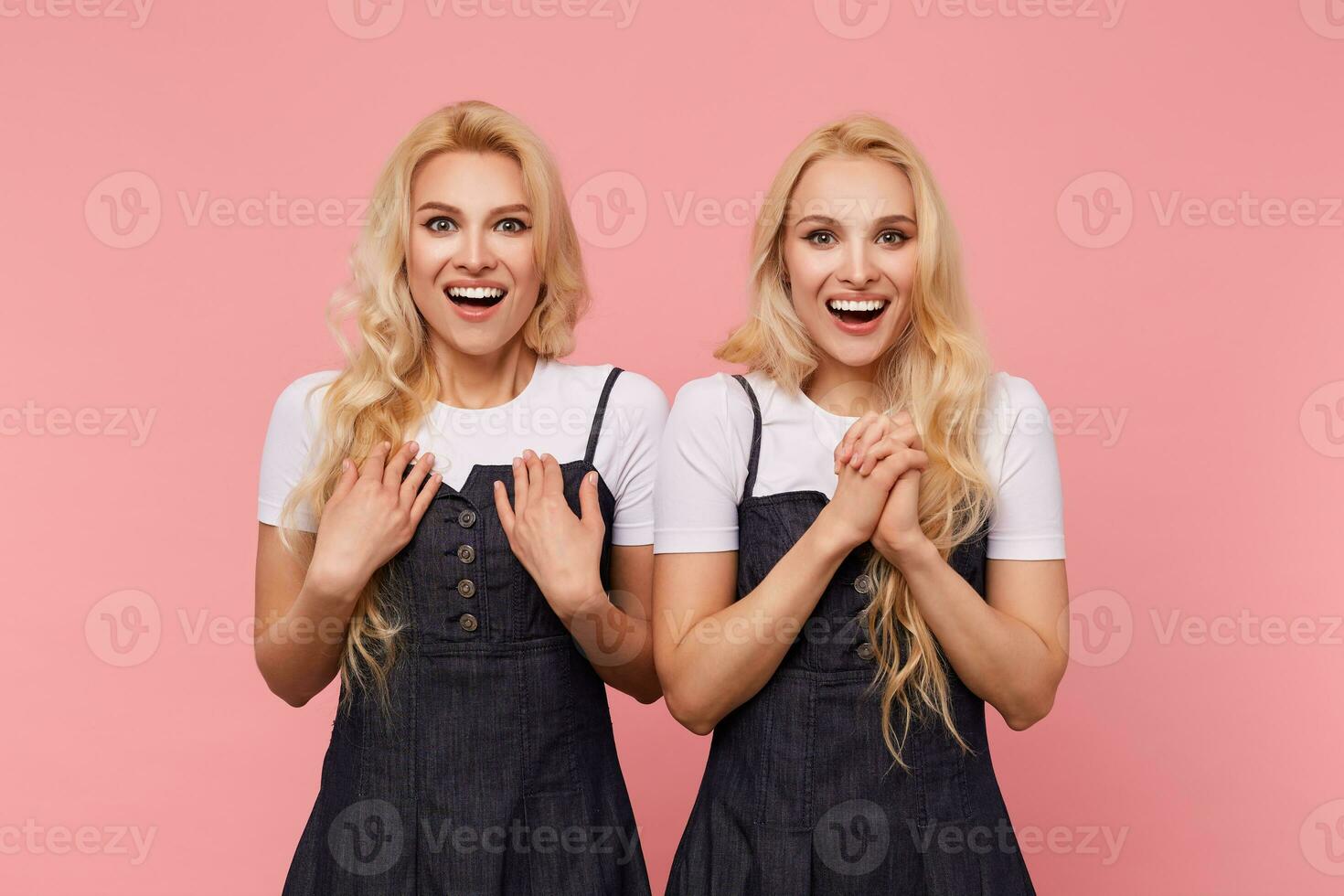 opgewonden jong lief lang haren blond Dames lachend vrolijk terwijl op zoek Bij camera en verhogen emotioneel handen, geïsoleerd over- roze achtergrond foto