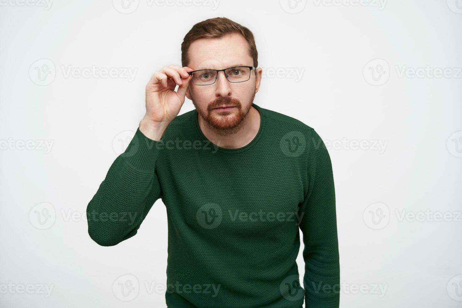 twijfelen jong brunette kort haren mooi mannetje met baard op zoek aandachtig Bij camera en Holding hand- Aan zijn brillen, poseren over- wit achtergrond in gewoontjes kleren foto