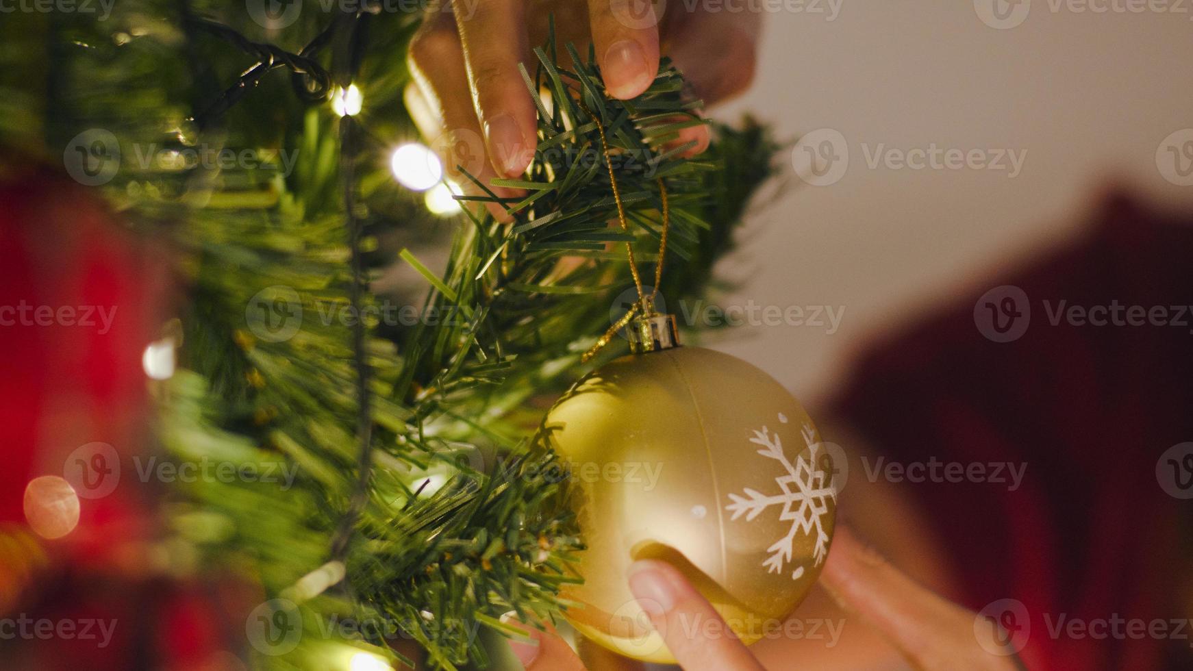 Aziatische vrouw versierd met ornament op kerstboom op kerstnacht en nieuwjaarsfestival thuis. kerstviering evenement voorbereiding of wintervakantie festival indoor party. Close-up shot. foto