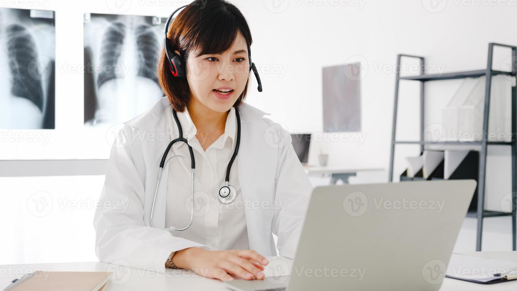 jonge Aziatische vrouwelijke arts in wit medisch uniform met stethoscoop met behulp van computerlaptop praten videoconferentiegesprek met patiënt aan balie in gezondheidskliniek of ziekenhuis. advies- en therapieconcept foto