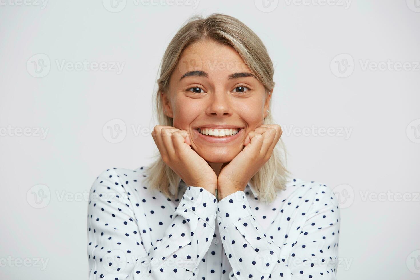 portret van glimlachen mooi blond jong vrouw draagt polka punt overhemd voelt gelukkig en looks direct in camera geïsoleerd over- wit achtergrond foto