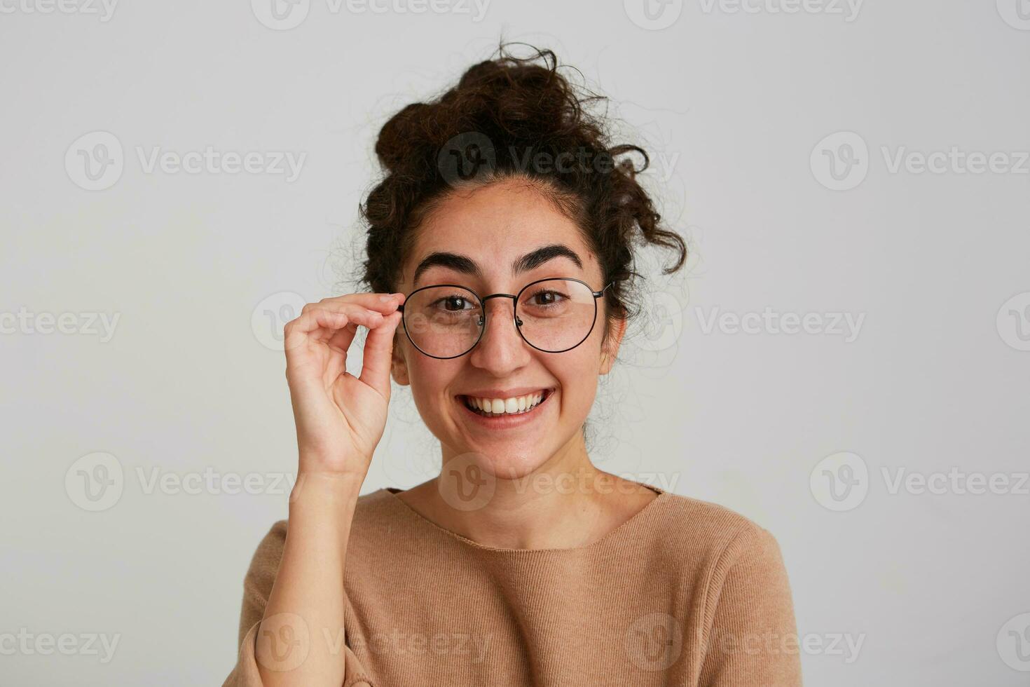 portret van vrolijk schattig Georgisch jong vrouw met gekruld haar- draagt beige stoppen en bril voelt gelukkig en lachend geïsoleerd over- wit achtergrond foto