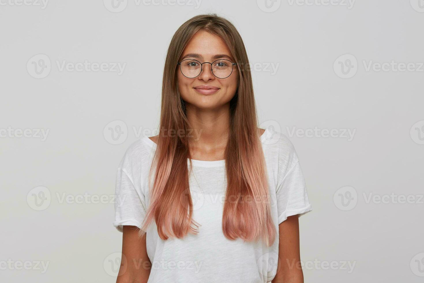 portret van glimlachen mooi jong vrouw leerling met lang geverfd pastel roze haar- draagt t overhemd en bril voelt gelukkig en zelfverzekerd geïsoleerd over- wit achtergrond looks direct in camera foto