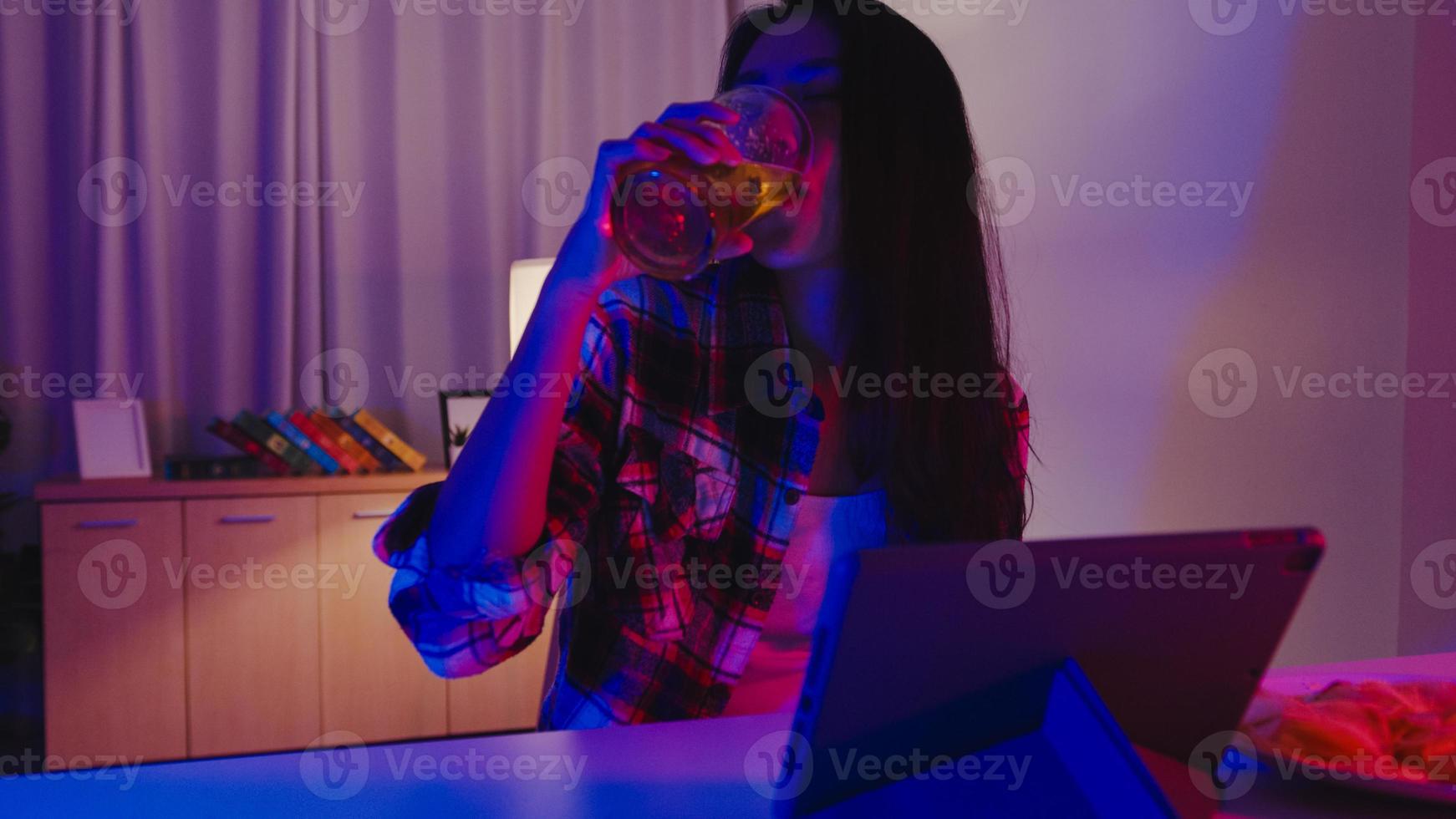 jonge azië dame bier drinken plezier gelukkig moment disco neon nacht feest evenement online viering via video-oproep in de woonkamer thuis. sociale afstand, quarantaine voor coronaviruspreventie. foto