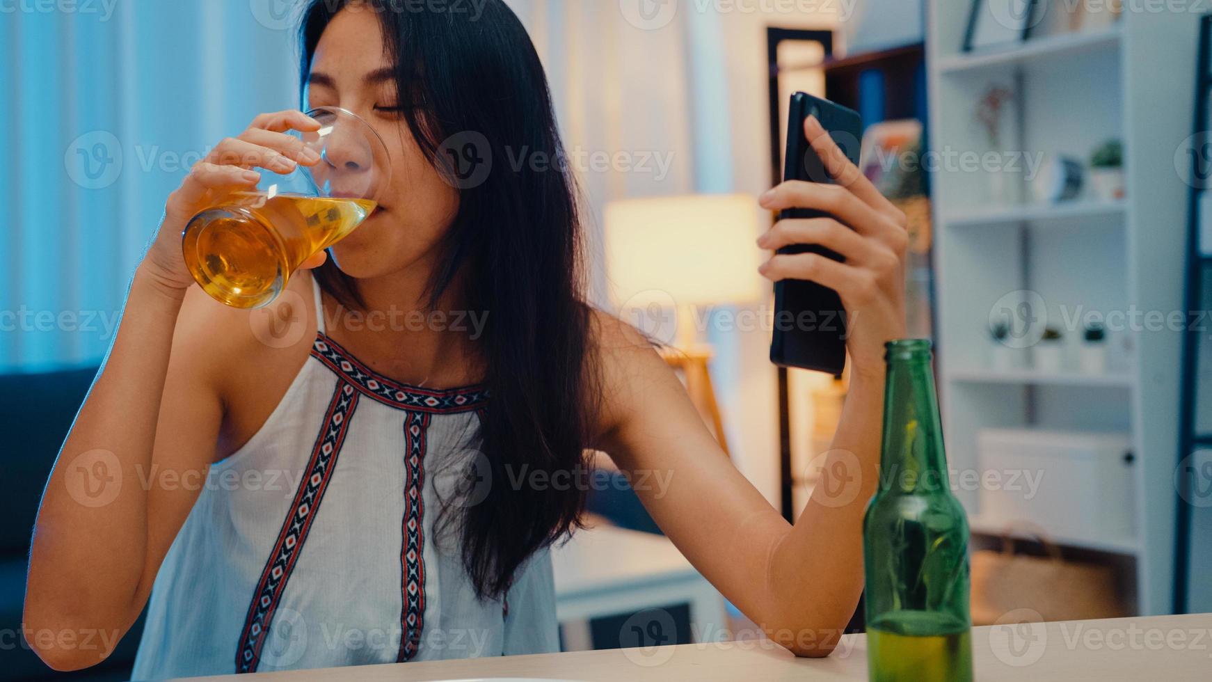 jonge azië dame bier drinken plezier gelukkig moment nacht feest nieuwjaar evenement online viering via video-oproep per telefoon thuis 's nachts. sociale afstand, quarantaine voor coronaviruspreventie. foto