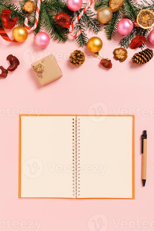 minimale creatieve platte lay van winterkerst traditionele compositie en nieuwjaarsvakantieseizoen. bovenaanzicht open mockup zwarte notebook voor tekst op roze achtergrond. bespotten en kopiëren van ruimtefotografie. foto