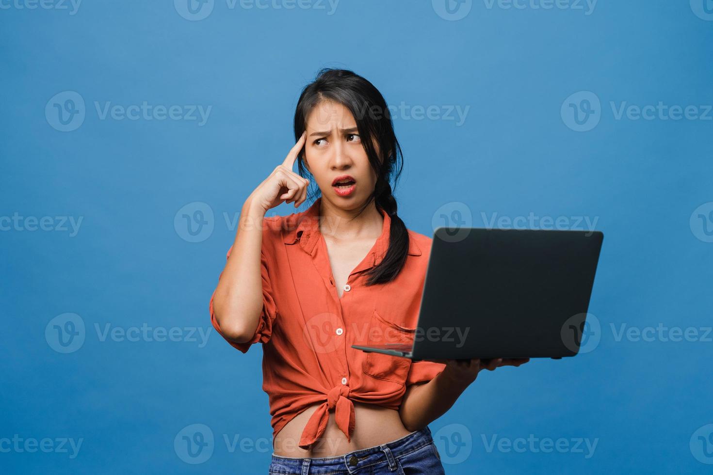 jonge Aziatische dame met behulp van laptop met negatieve uitdrukking, opgewonden schreeuwen, huilen emotioneel boos in casual doek en staan geïsoleerd op blauwe achtergrond met lege kopie ruimte. gezichtsuitdrukking concept. foto